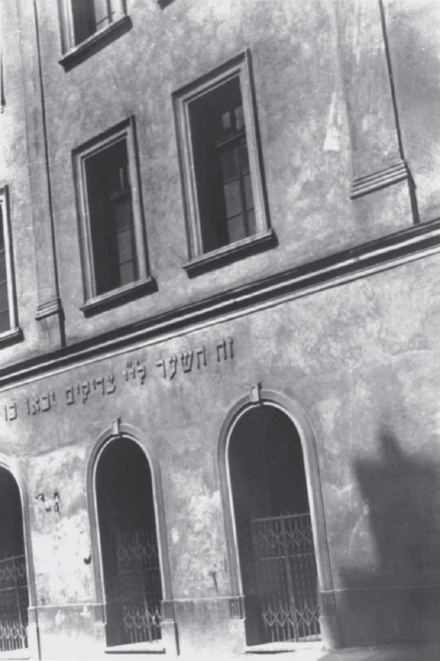 Schwarzes und weißes Foto eines Gebäudes in Jerusalem mit Fenstern, Türen und einem Metallzaun, das mutmaßlich eine jüdische Synagoge ist.