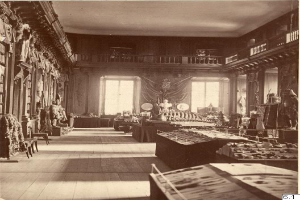 Ein altes Schwarz-Weiß-Foto eines Raumes voller Tische, Stühle, Skulpturen an den Wänden, Fenstern, Vorhängen, Geländern und anderen Gegenständen mit der Aufschrift "Museum of Fine Arts, London" unten.