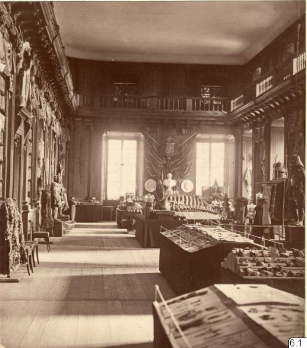 Ein altes Schwarz-Weiß-Foto eines Raumes voller Tische, Stühle, Skulpturen an den Wänden, Fenstern, Vorhängen, Geländern und anderen Gegenständen mit der Aufschrift "Museum of Fine Arts, London" unten.