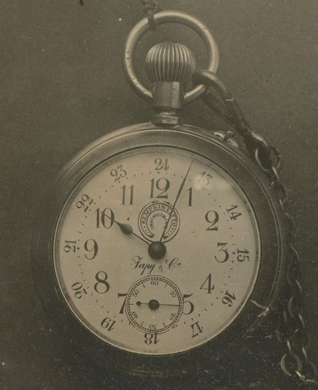 Altes Schwarz-Weiß-Foto einer Taschenuhr mit einer Kette, das ein nummeriertes Zifferblatt zeigt.